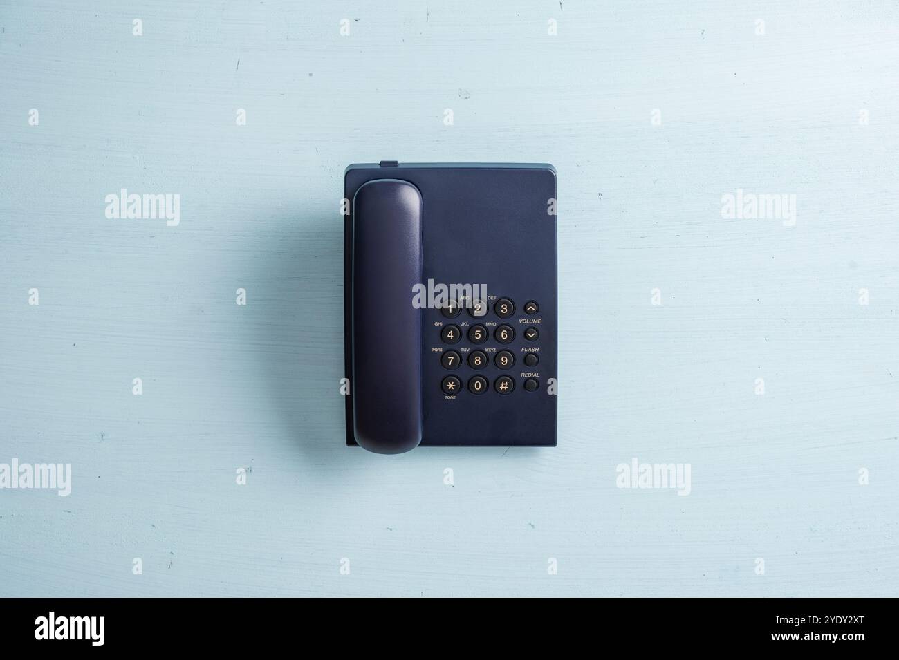 Ein klassisches, schwarzes schnurgebundenes Telefon mit Wählscheibe auf einer hellblauen Holzoberfläche, das eine nostalgische Atmosphäre der Retro-Kommunikation hervorruft. Stockfoto