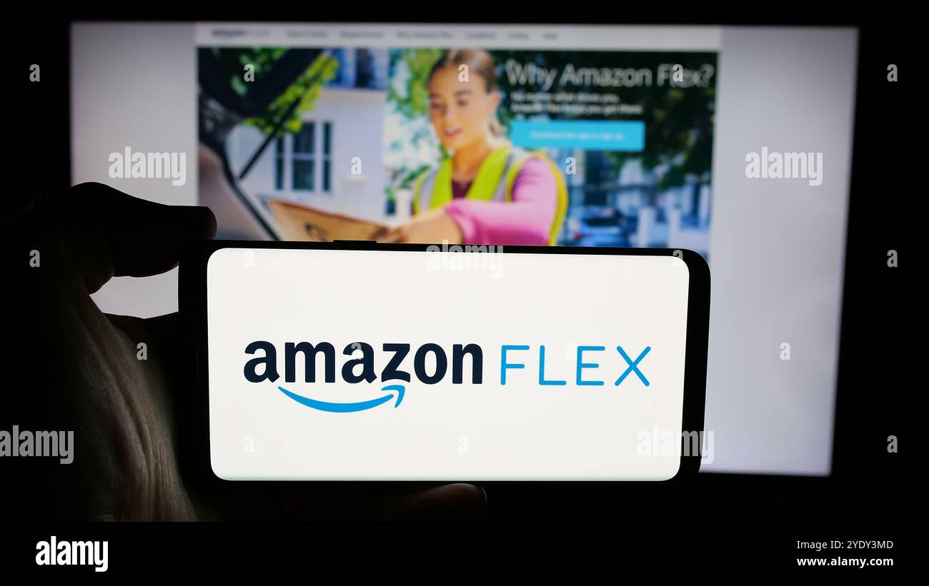 Person, die ein Mobiltelefon mit dem Logo des Zustellfahrerprogramms Amazon Flex auf dem Bildschirm vor der Unternehmenswebseite hält. Schwerpunkt auf dem Display des Telefons. Stockfoto
