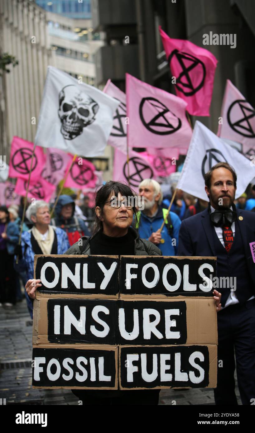 London, England, Großbritannien. Oktober 2024. Demonstranten marschieren durch die Stadt, man trägt ein Schild mit der Aufschrift „˜nur Narren versichern fossile Brennstoffe“. Extinction Rebellion (XR) spazieren Sie durch die City of London, halten Sie an und demonstrieren Sie vor den Büros von Versicherungsunternehmen, die trotz der Warnungen vor einer Klimakrise von Wissenschaftlern weiterhin Unternehmen für fossile Brennstoffe versichern. Die Demonstranten glauben, wenn die Versicherungsgesellschaften ihre Beteiligung an diesen Unternehmen beenden würden, würden sie es schwer tun, weiter zu bauen. Die Aktion ist die erste einer Woche lang, die sich speziell gegen die Versicherungsgesellschaft richtet Stockfoto