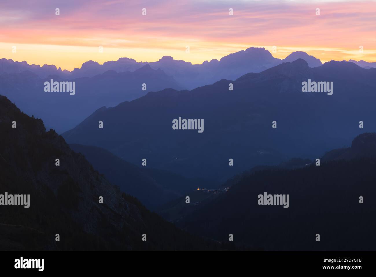 Twilight view of the Italian Dolomites from Giau Pass, with a colorful sunset sky illuminating the rugged mountains and a distant village Selva di Cad Stockfoto