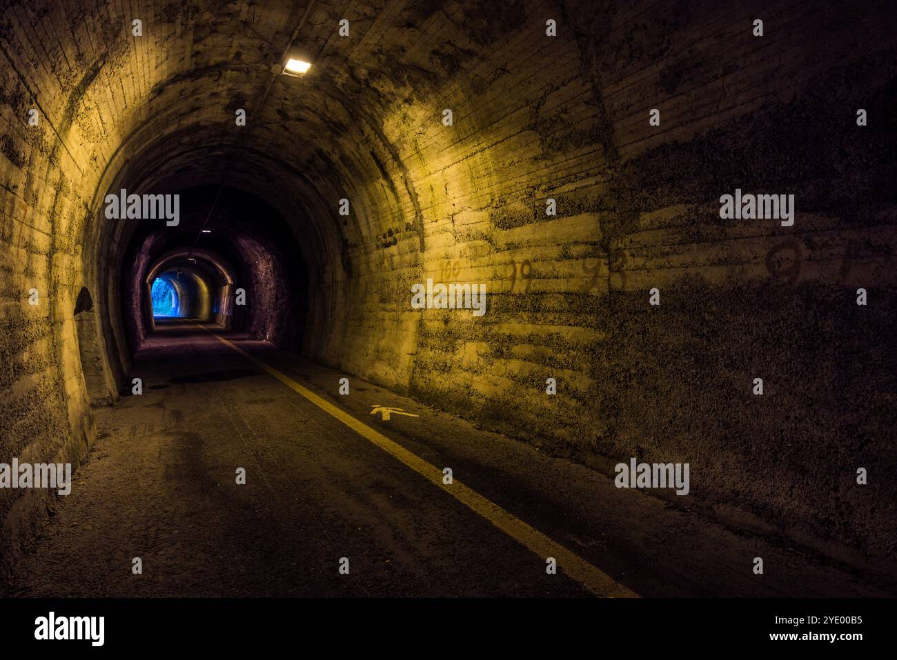 Bemalte Entfernungsmarkierungen und ein Richtungspfeil kennzeichnen die Wand eines der ehemaligen Eisenbahntunnel in der Nähe von Borgo Maggiore; Tageslicht ist am anderen Ende des gewölbten Durchgangs wieder sichtbar. Via Paolo Amaducci, Borgo Maggiore, San Marino. Stockfoto