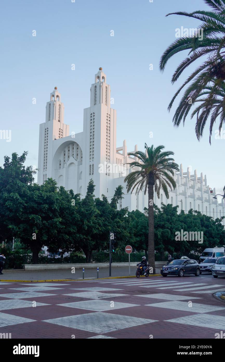 Eine große, weiße, reich verzierte Kathedrale namens „sacré coeur“ mit zwei hohen Türmen, umgeben von üppigen grünen Bäumen und Palmen, mit einem karierten Pflaster Stockfoto