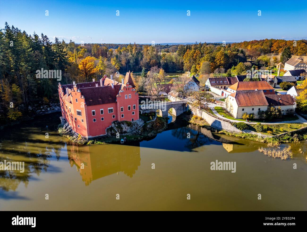 Ein Panorama-Drohnenfoto von Schloss Cervena Lhota (Rotes Schloss, Schloss Rot), das die Reflexion der Burg im Teich darunter zeigt. Umgeben von Herbst-Co Stockfoto