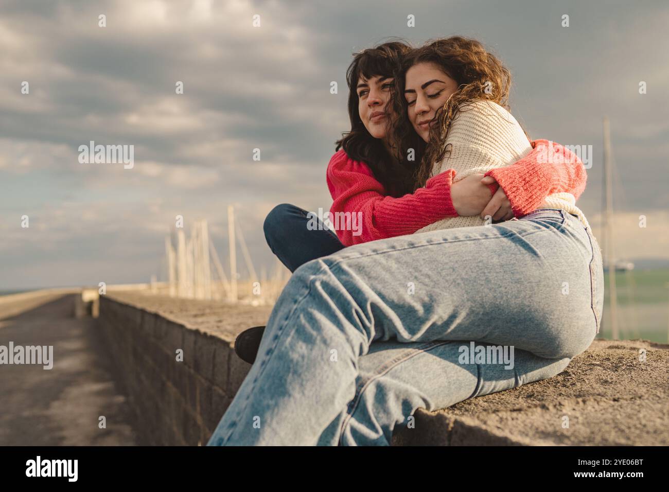 Der natürliche Moment von Freunden der Generation Z, die sich auf die Stadtmauer umarmen. Junge, vielfältige Frauen, die authentische Momente der Verbindung, echte Freundschaft und Unterstützung teilen Stockfoto