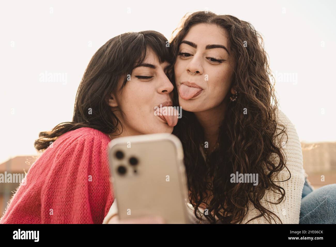 Authentischer Moment, in dem verschiedene Freunde der Generation Z Selfie im Freien machen. Junge Frauen mit lockigen Haaren und Zahnspangen, die lustige Gesichter an der Smartphone-Kamera machen, echt Stockfoto