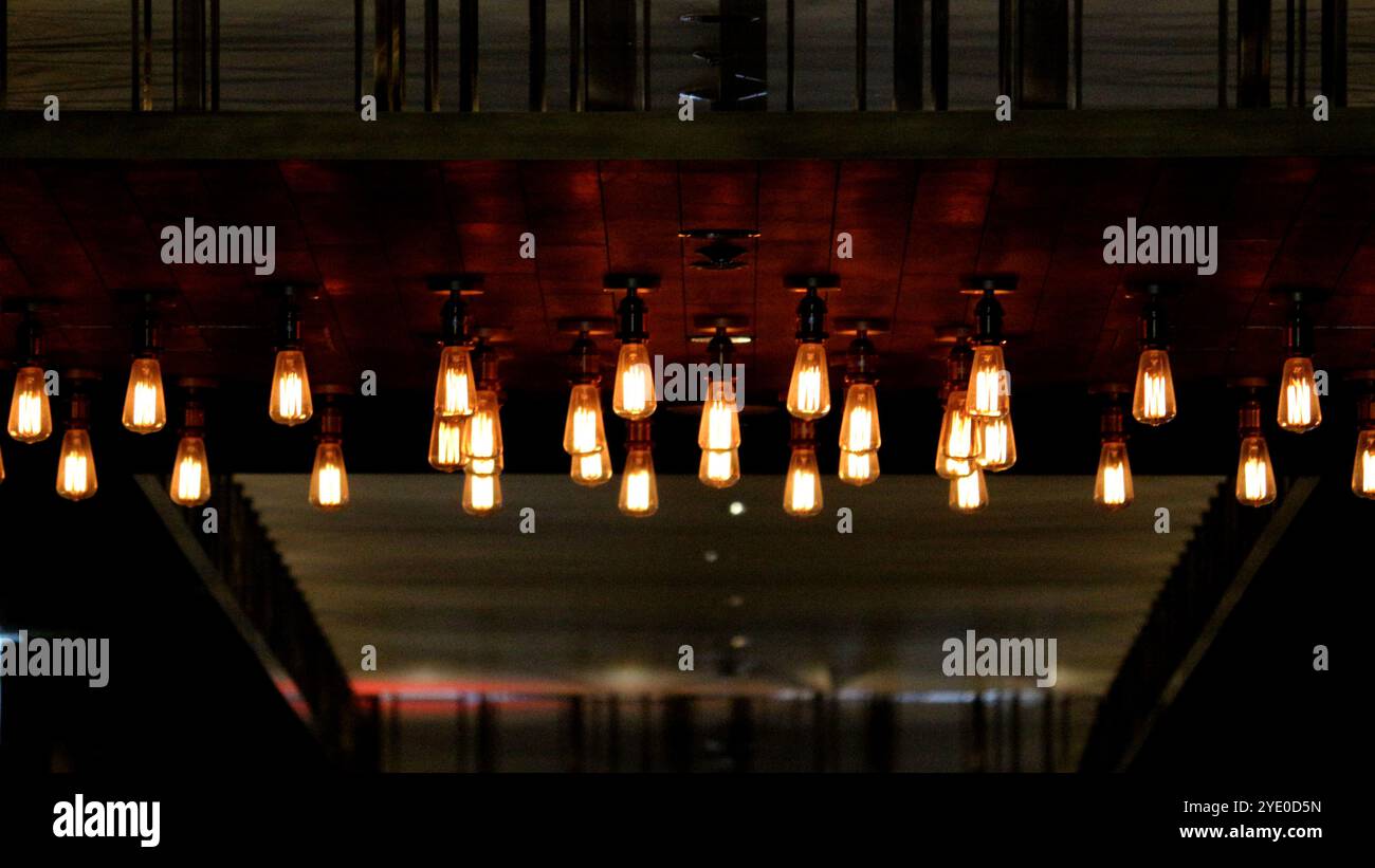Mehrere einfach gestaltete Pendelleuchten hängen von der Decke in einem schwach beleuchteten Raum Stockfoto