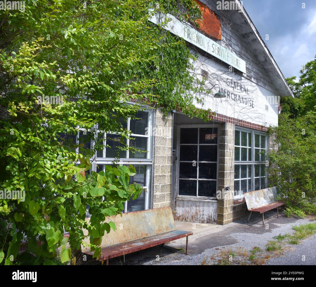 Zwei rostende Bänke aus Metall sitzen vor einem alten Laden auf dem Land. Es ist nicht mehr in Betrieb, aber Worte über Bänken werben für freundlichen Service und Stockfoto