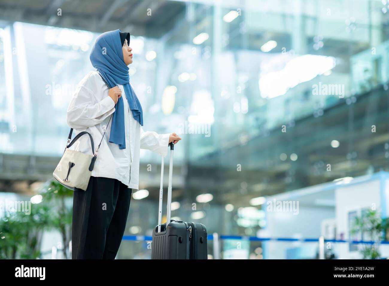 Eine asiatische Muslimin mit blauem Hijab bereitet sich auf einen Urlaub vor und sie ist am Flughafen. Sie wartet auf ihre Freunde, muslimische Reisende. Stockfoto