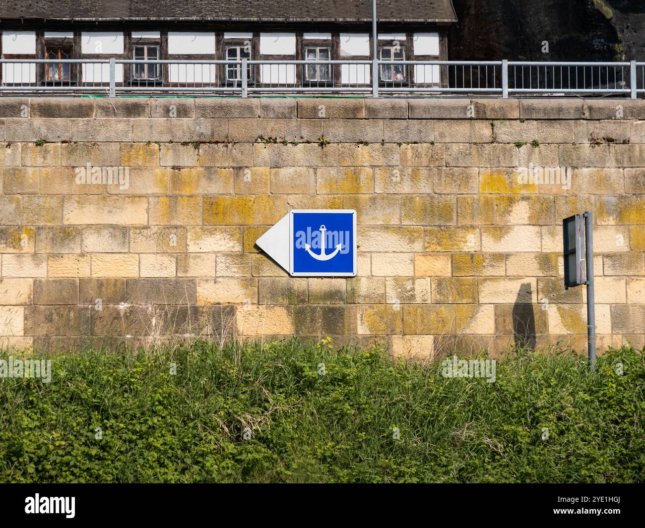 Ankern Sie das Verkehrsschild, das an einer Mauer neben einem Fluss angebracht ist. Das Pfeilsymbol führt Bootsfahrer zu einem Ort, an dem sie den Anker ablegen können. Stockfoto