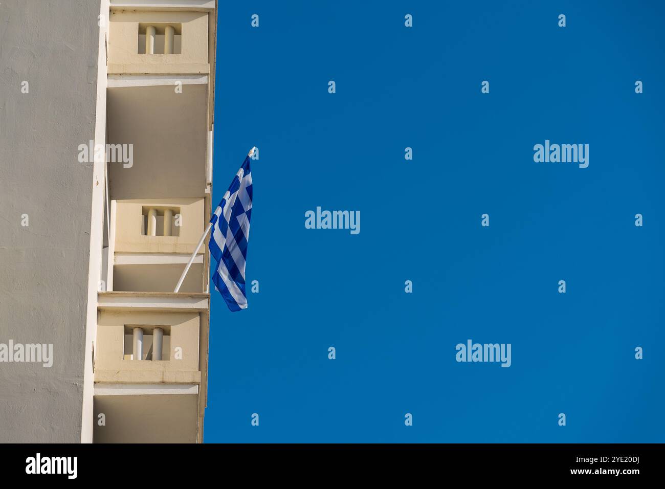 Gelbe Balkone und griechische Flagge vor dem klaren blauen Himmel: Eine Hommage an den Feiertag Stockfoto