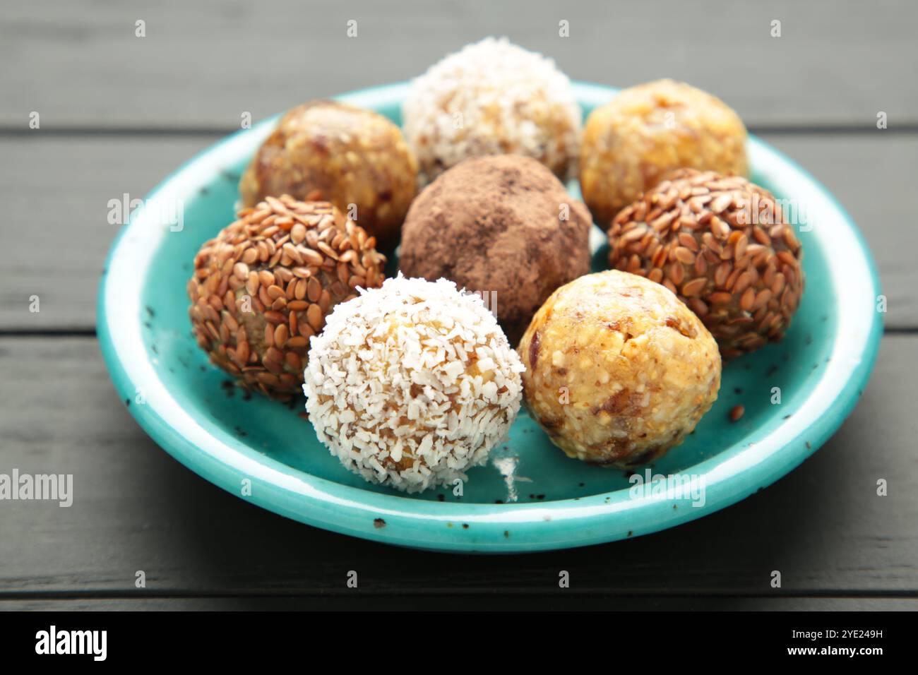 Gesunde hausgemachte Energiebälle mit Preiselbeeren, Nüssen, Datteln und Haferflocken auf blauer Platte auf schwarzem Hintergrund. Draufsicht Stockfoto