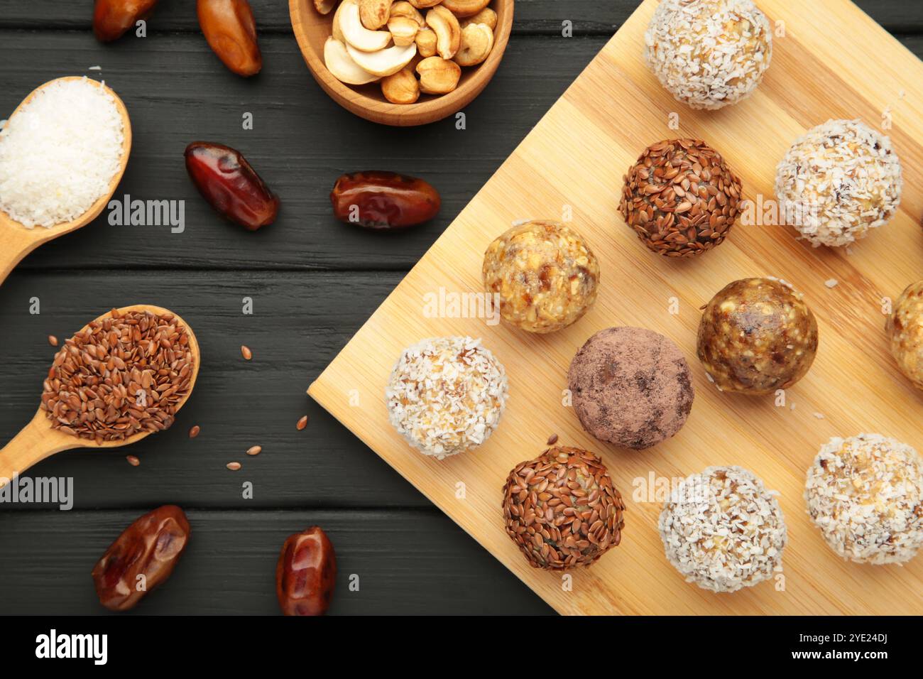 Gesunde hausgemachte Energiebälle mit Preiselbeeren, Nüssen, Datteln und Haferflocken auf Schneidebrett auf schwarzem Hintergrund. Draufsicht Stockfoto