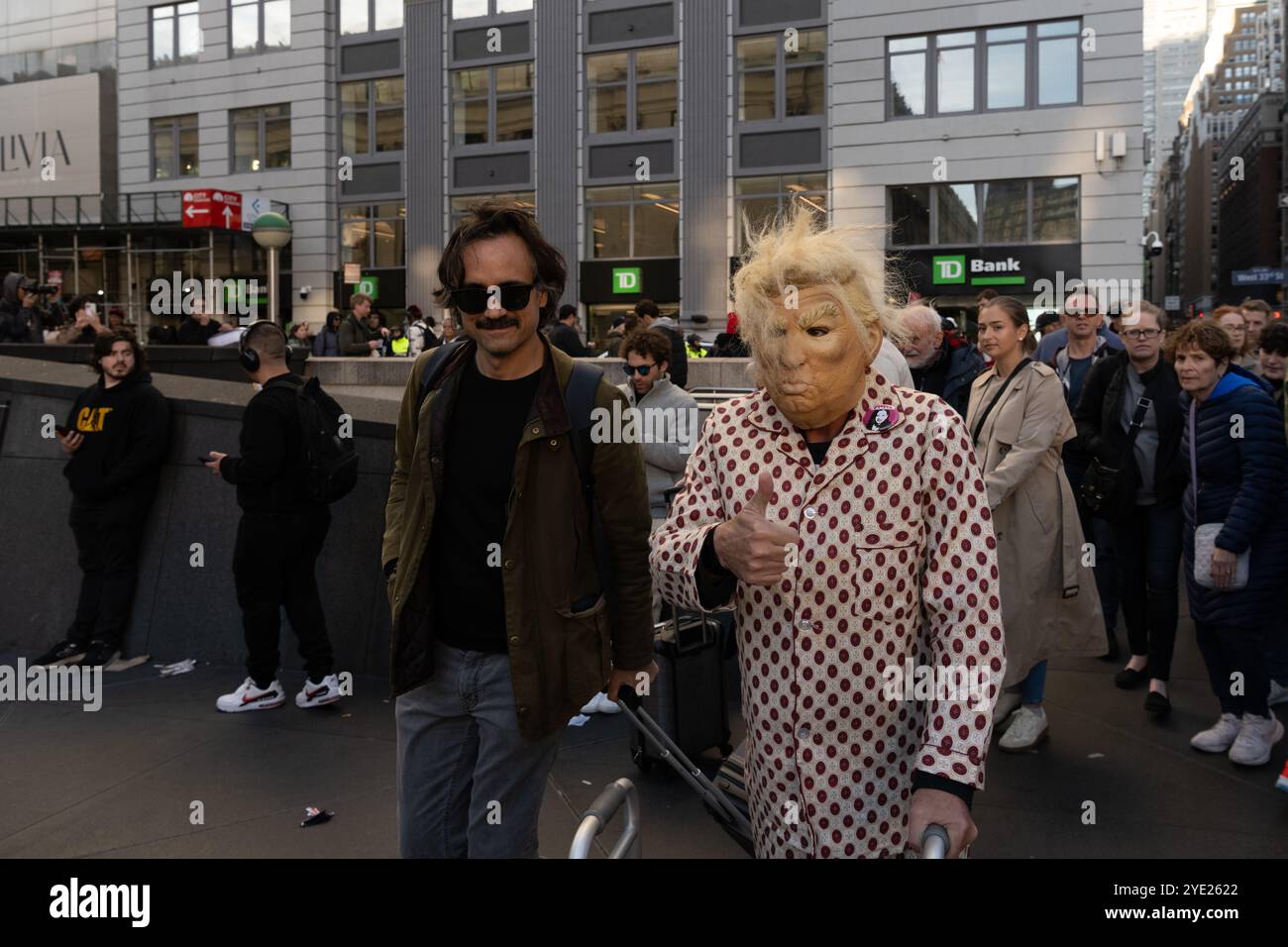 Eine Person, die eine Donald Trump Maske und eine Kamala Harris Pin trägt, läuft gegenüber von Donald Trumps Kundgebung im Madison Square Garden. Stockfoto