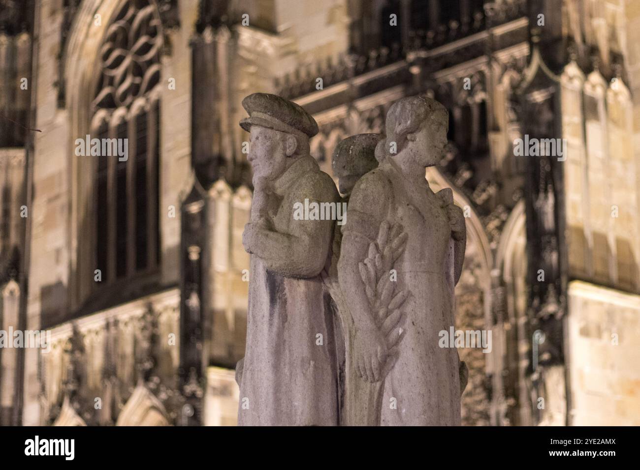 Ein nächtlicher Blick auf den Münster Dom mit einer wunderschön beleuchteten Steinskulptur im Vordergrund, die den gotischen Charme und die komplizierten Details von unterstreicht Stockfoto