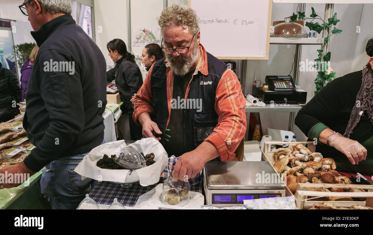 Beim Alba-Trüffelfestival in Italien wiegt und verpackt ein Händler gekonnt frische Trüffel, während er von eifrigen Kunden umgeben ist. Stockfoto