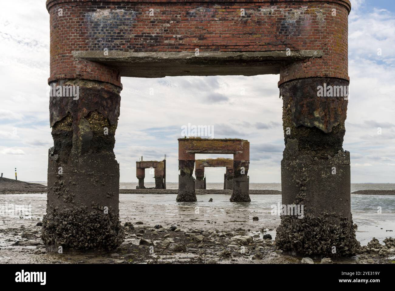 Rostige, verwitterte Überreste des alten Piers an der Eckwarderhörne, mit robusten Ziegelsäulen bedeckt, die bei Ebbe freigelegt sind. Stockfoto