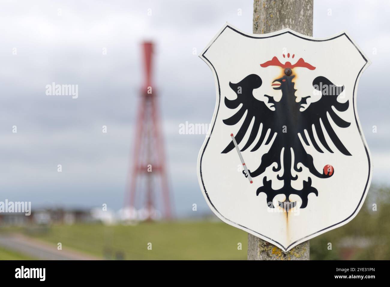 Nahaufnahme eines deutschen Grenzschilds mit einem kaiserlichen Adlersymbol mit dem berühmten roten Obelisk Leuchtturm in Eckwarderhörne, Deutschland. Stockfoto