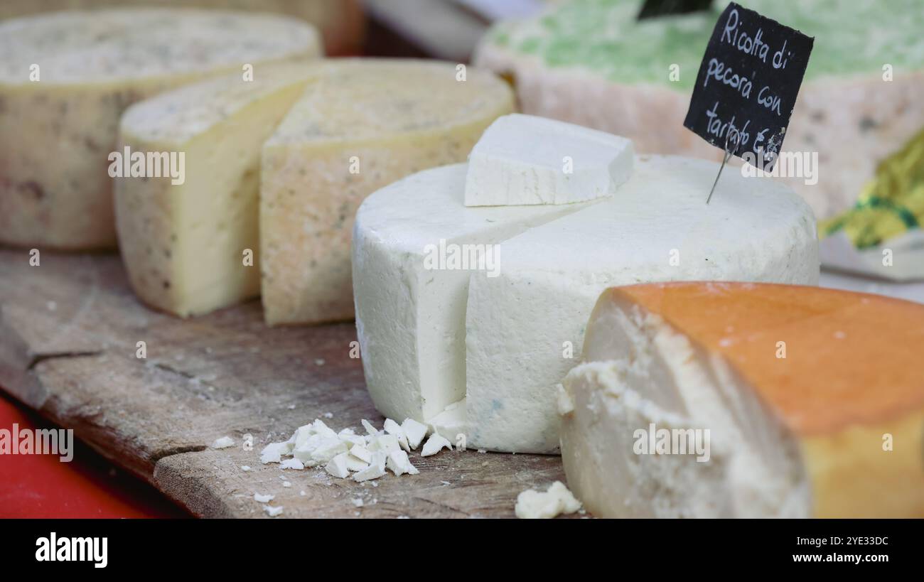 Eine Auswahl handwerklicher Käsesorten wird auf einem Holzbrett auf einem geschäftigen Markt in Alba, Italien, präsentiert. Jeder Käse ist einzigartig geformt Stockfoto Eine Auswahl handwerklicher Käsesorten wird auf einem Holzbrett auf einem geschäftigen Markt in Alba, Italien, präsentiert. Jeder Käse ist einzigartig geformt Stockfoto