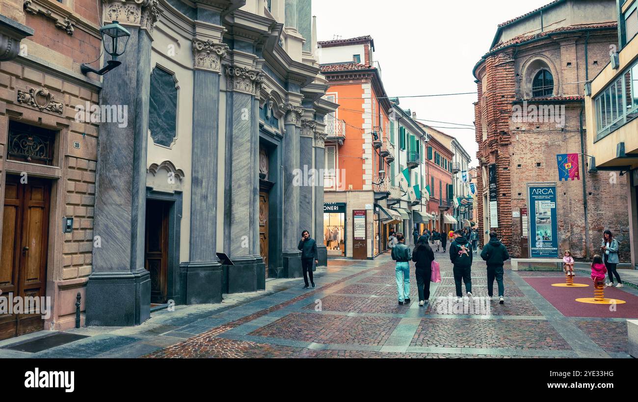 Besucher spazieren durch die kopfsteingepflasterten Straßen von Alba, Italien, und bewundern die historischen Gebäude, pulsierenden Geschäfte und die herrliche Atmosphäre Stockfoto