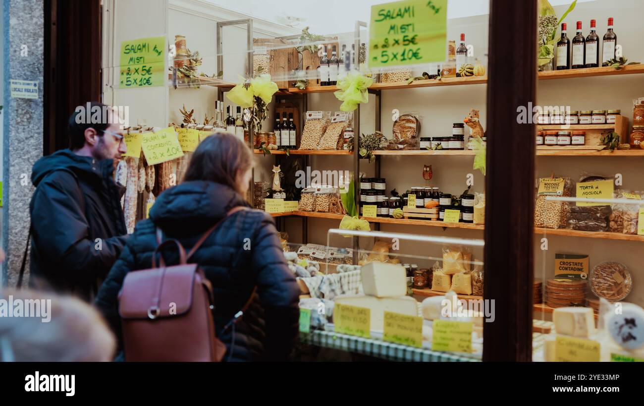 Ein Paar stöbert in einem Kunsthandwerksgeschäft in Alba, Italien, das von einer Vielzahl von Salami, lokalen Käsesorten und hausgemachten Köstlichkeiten fasziniert ist Stockfoto