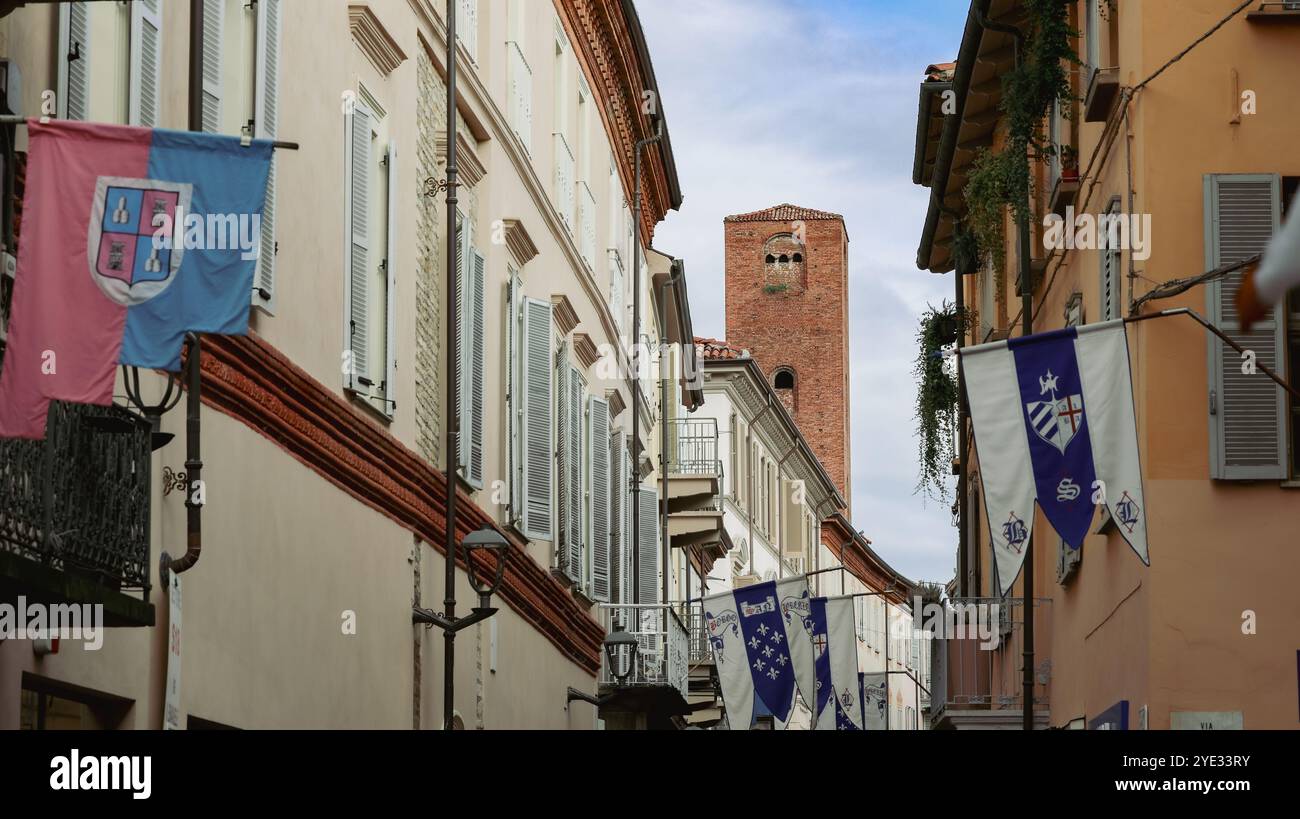 Im Herzen von Alba, Italien, zeigt eine alte Gasse wunderschöne Architektur mit bunten Bannern, die einen Einblick in die reiche Geschichte der Städte zeigen Stockfoto