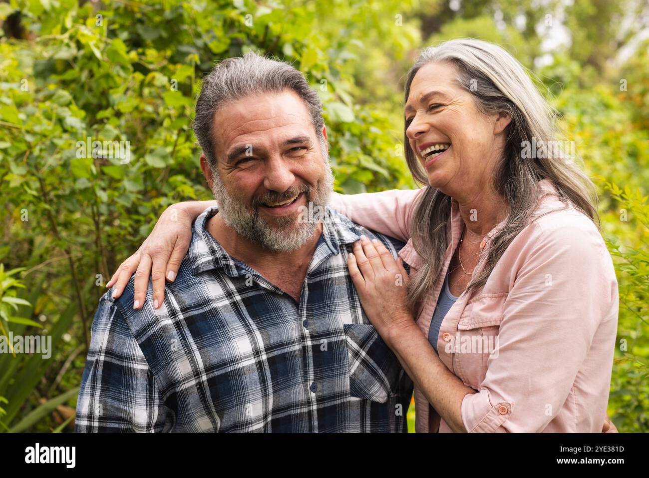 Glückliches, reifes Paar lacht zusammen im üppigen Garten und genießt Outdoor-Momente Stockfoto