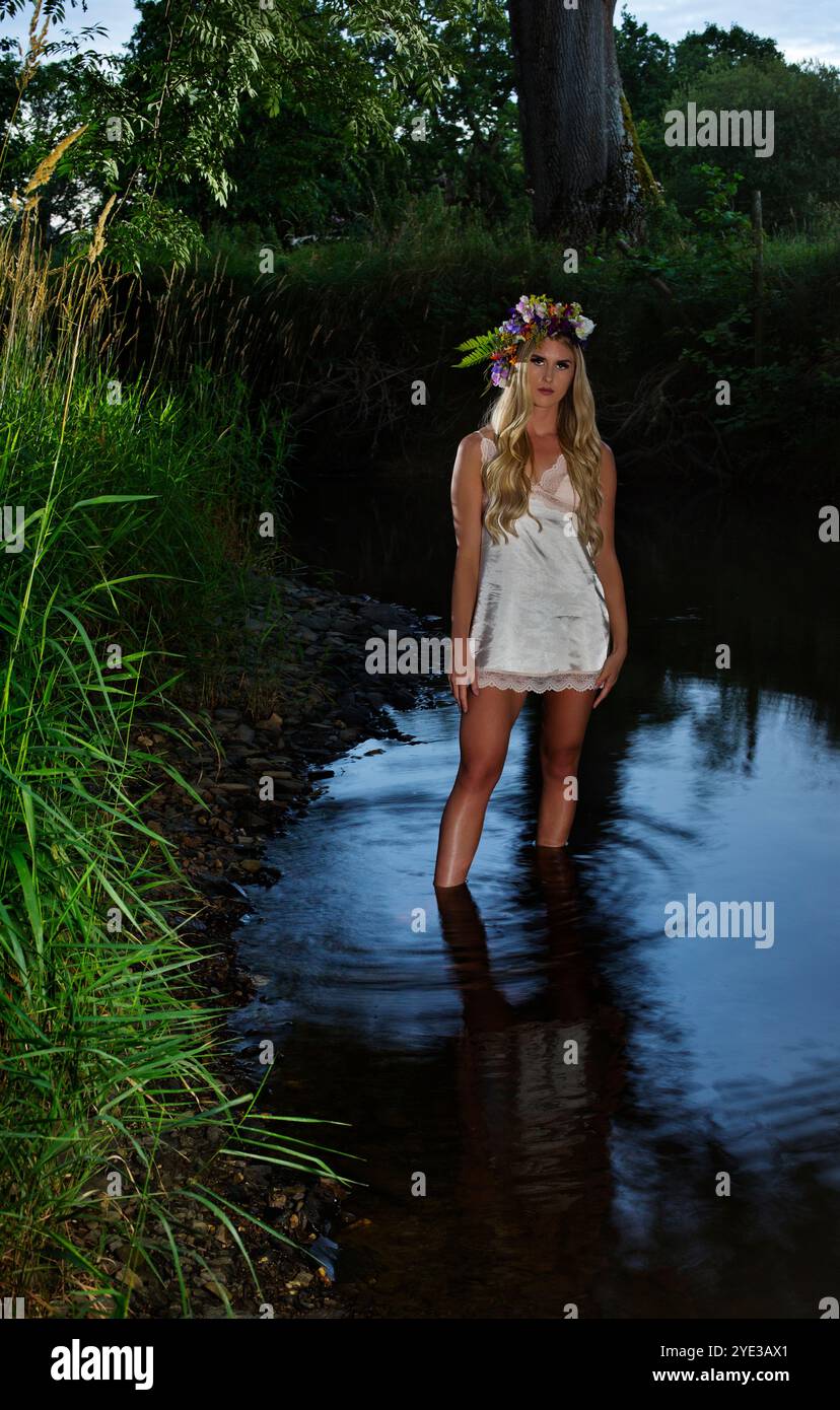 Eine schöne blonde Frau, die in der Abenddämmerung in einem Fluss steht Stockfoto