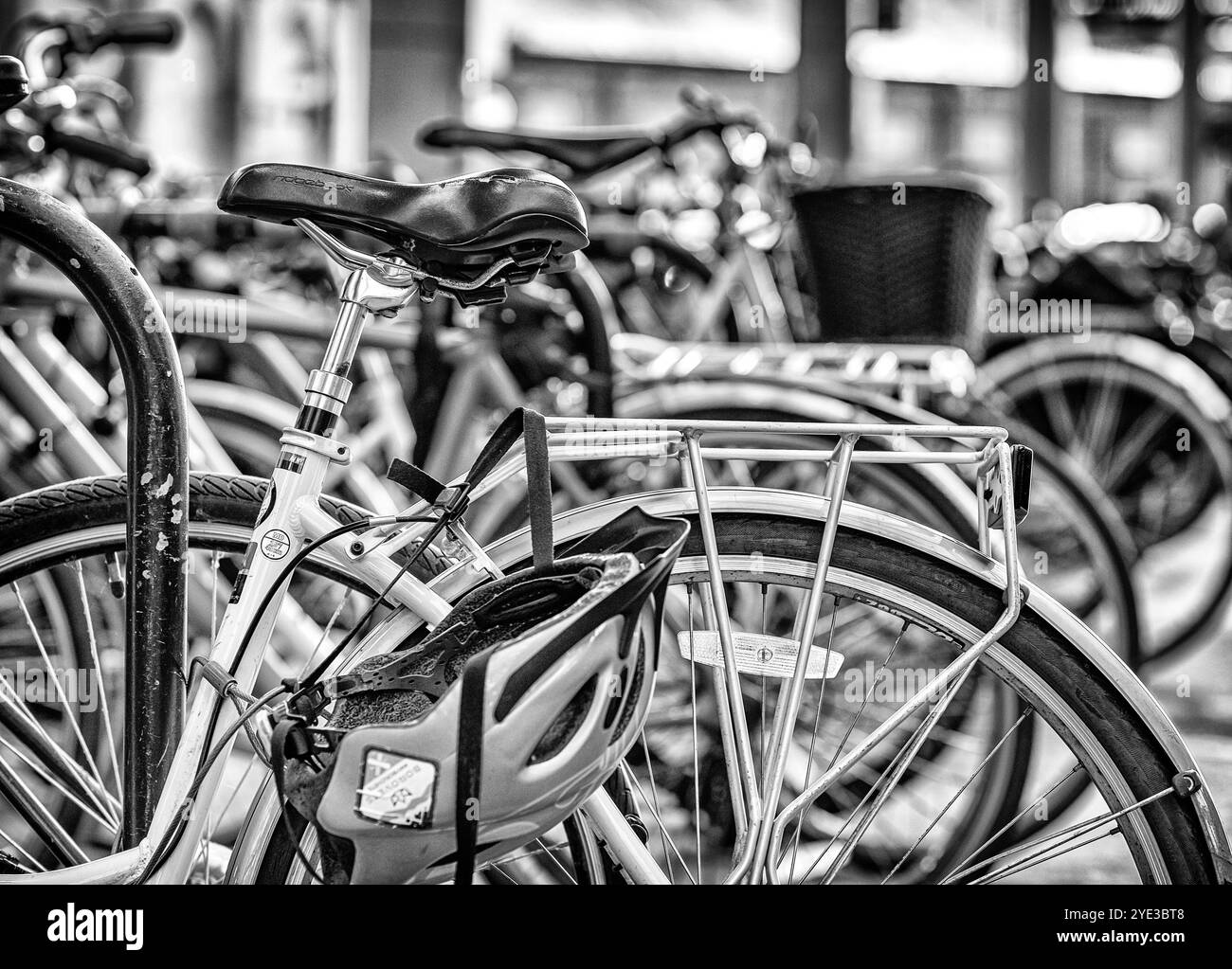 Ein Fahrrad in einem Fahrradträger am Bahnhof. Der Sattel wird getragen und ein Helm hängt am Träger. Eine Reihe von Fahrrädern befindet sich im Hintergrund. Stockfoto