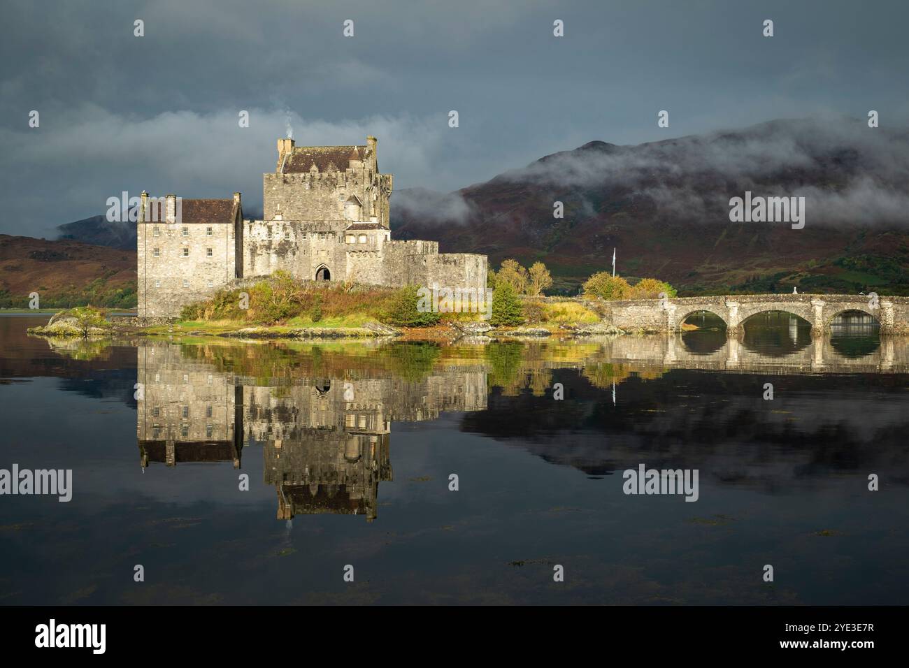 Das Sonnenlicht beleuchtet Eilean Donan Castle, das sich im Loch Duich mit Scotch-Nebel im Hang hinter den Highlands, Schottland, spiegelt Stockfoto