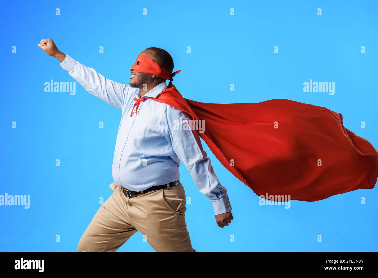 Afroamerikaner übergewichtiger Typ im superman Kostüm, in fliegender Pose auf blauem Hintergrund, Konzept von Geschwindigkeit, Superkräften und Superfähigkeiten Stockfoto