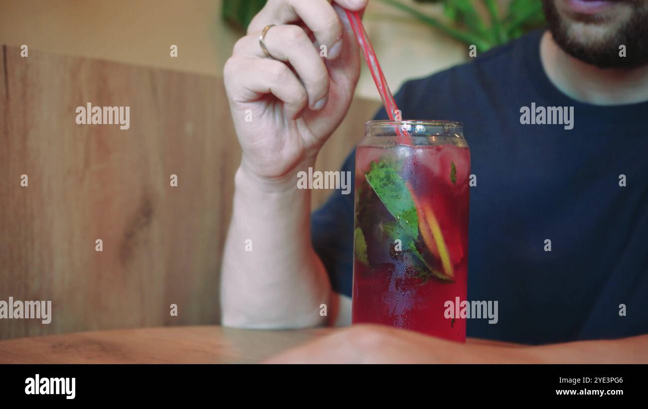 Eine friedliche Szene entfaltet sich, während sich der Mann bei einem Sommerdrink entspannt. Seine Auswahl an Getränken und seine Umgebung ergänzen seinen ruhigen Moment perfekt. Das gemütliche Café Stockfoto