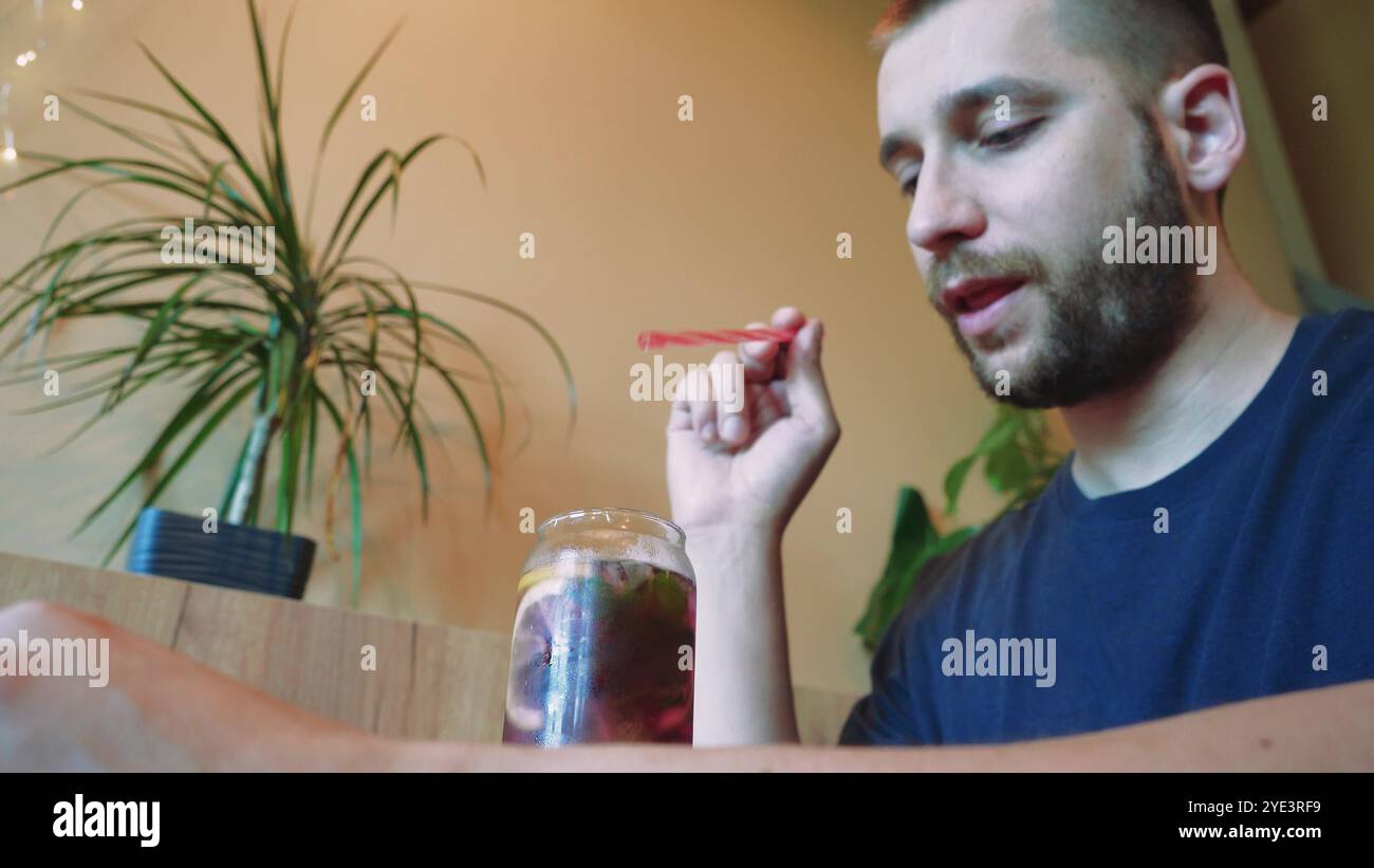 Bei einem kühlen Cocktail spürt der junge Mann die Sommeratmosphäre. Blumen in Vasen im Hintergrund schaffen eine ruhige Atmosphäre für diese Erfrischung Stockfoto