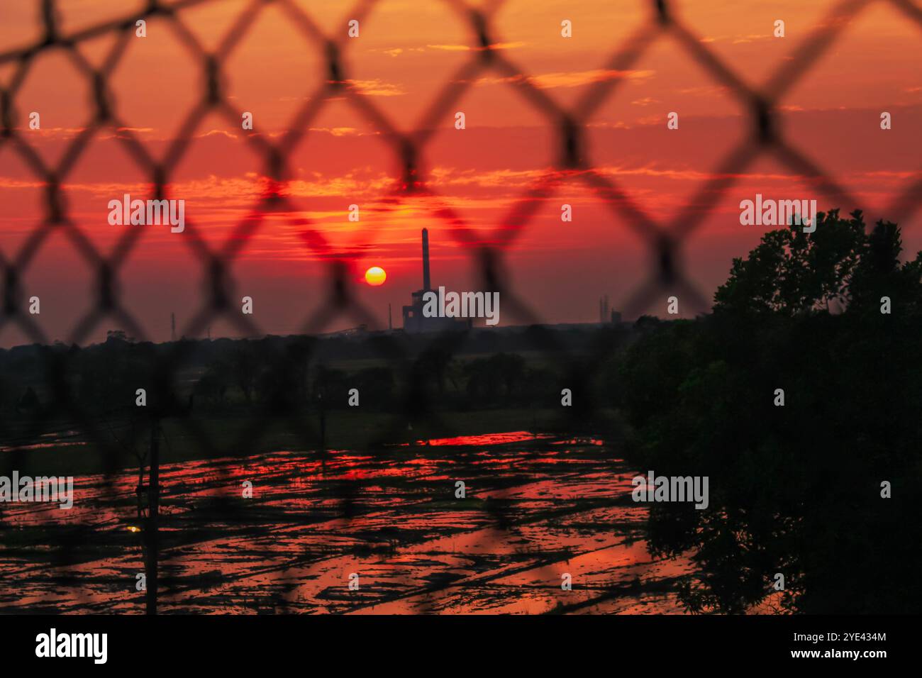 Die Sonne und die Fabrik in der Silhouette am Morgen vor dem Kettenzaun Stockfoto