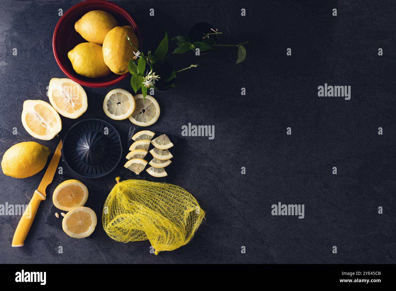 Elegantes Hintergrunddesign aus Zitronen und Zitronenscheiben mit Quetschpresse und Messer auf dunkler oder schwarzer Zement- oder Steinoberfläche.Draufsicht mit Kopierraum. Stockfoto