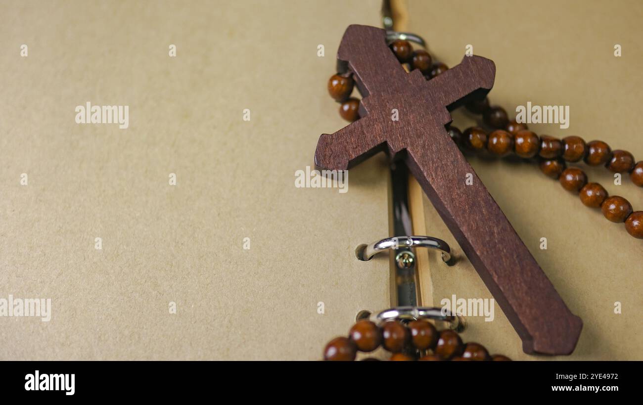 Dunkelrotes Holzkreuz, das sich an ein altes offenes Buch lehnt, das die Verbreitung der Liebe Jesu Christi unter Christen symbolisiert, die den Glauben und die Hingabe widerspiegelt Stockfoto