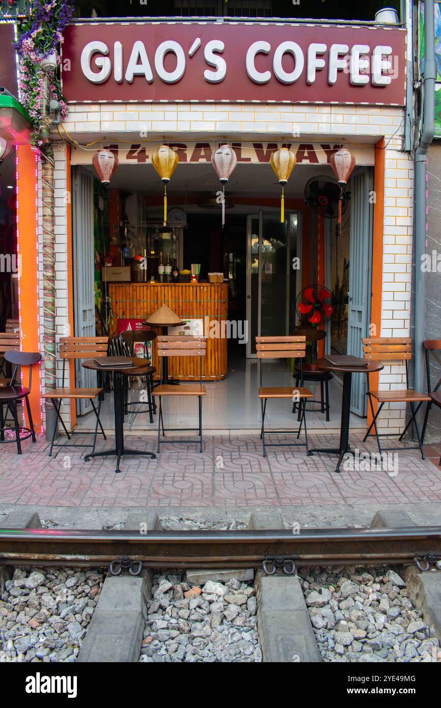 Vietnam: Hanoi Train Street, schmale Bahnumgehung, an der täglich Züge in der Nähe von Gebäuden auf beiden Seiten der Gleise vorbeifahren und Menschen trinken Stockfoto