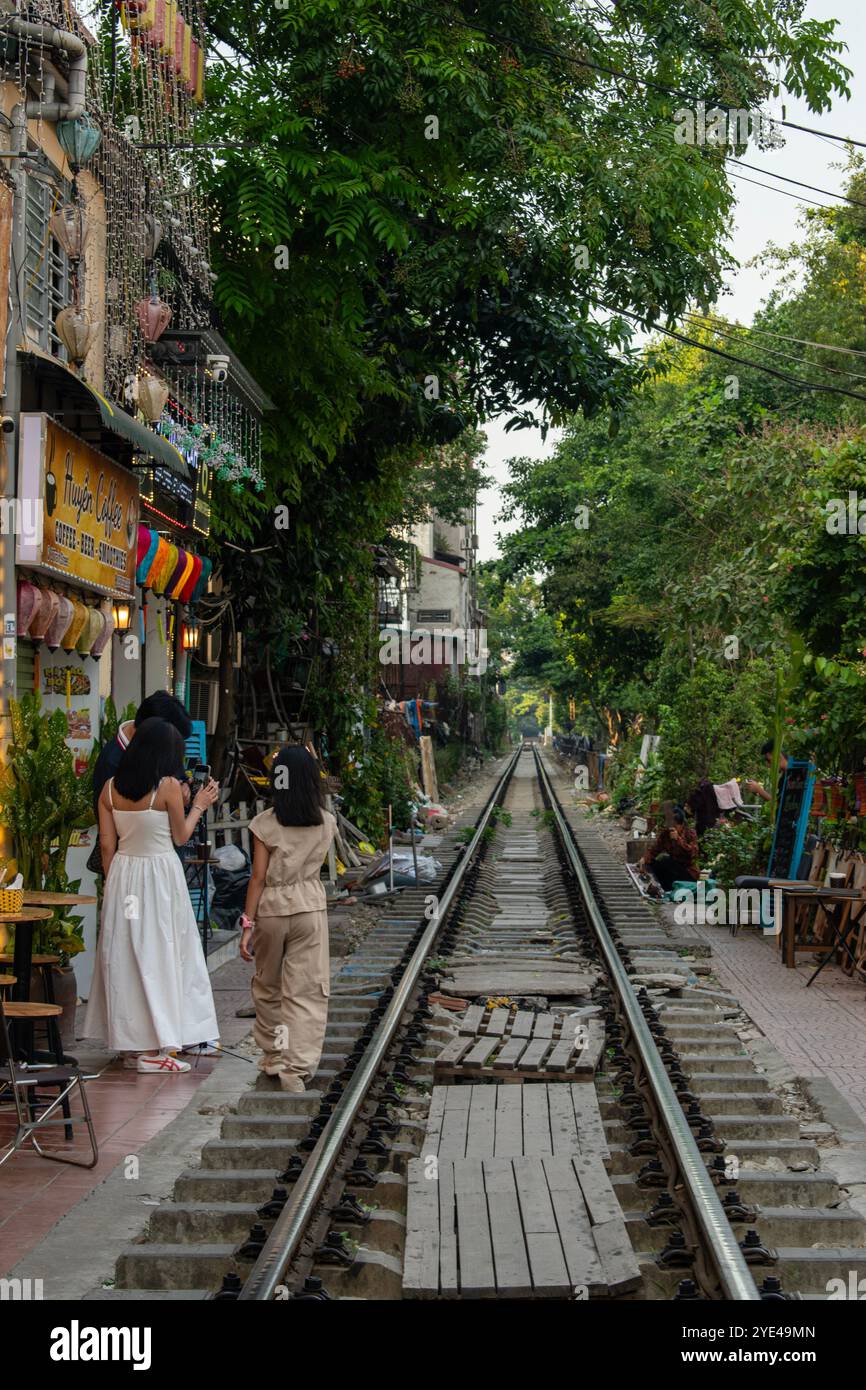 Vietnam: Hanoi Train Street, schmale Bahnumgehung, an der täglich Züge in der Nähe von Gebäuden auf beiden Seiten der Gleise vorbeifahren und Menschen trinken Stockfoto