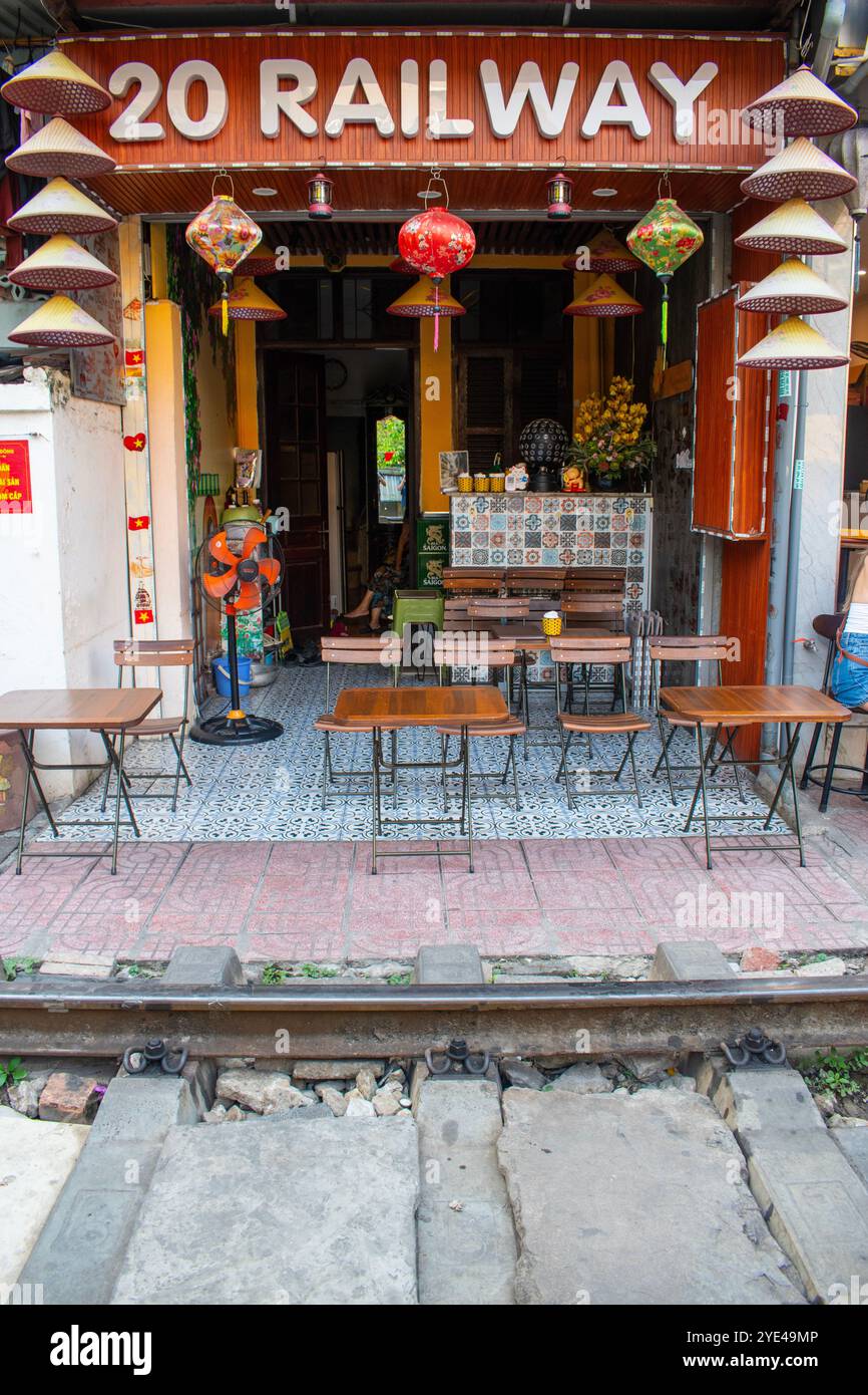 Vietnam: Hanoi Train Street, schmale Bahnumgehung, an der täglich Züge in der Nähe von Gebäuden auf beiden Seiten der Gleise vorbeifahren und Menschen trinken Stockfoto