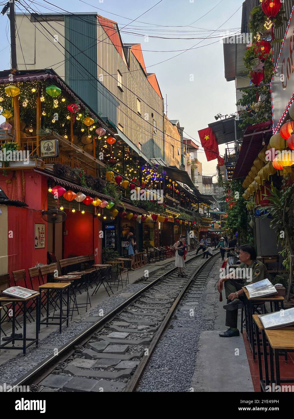 Vietnam: Hanoi Train Street, schmale Bahnumgehung, an der täglich Züge in der Nähe von Gebäuden auf beiden Seiten der Gleise vorbeifahren und Menschen trinken Stockfoto