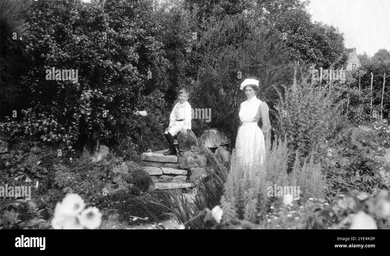 West Sussex, England. 1913: Ein kleiner Junge, der vermutlich ein Verwandter der Familie Henty ist, und sein Kindermädchen stehen in den Gärten auf dem Gelände von Ferring Grange in Ferring, einem Küstendorf in West Sussex. Das Anwesen war das Zuhause von Edwin Henty, J. P, D.L., F.S.A. (1844–1916), der als High Sheriff of Sussex gedient hatte. 1924 wurde das Haus in ein modisches Hotel umgewandelt, das von vielen Prominenten besucht wurde, darunter Edward, dem Prinzen von Wales (später bekannt als Duke of Windsor). Das Haus wurde im Oktober 1946 durch einen Brand zerstört. Stockfoto