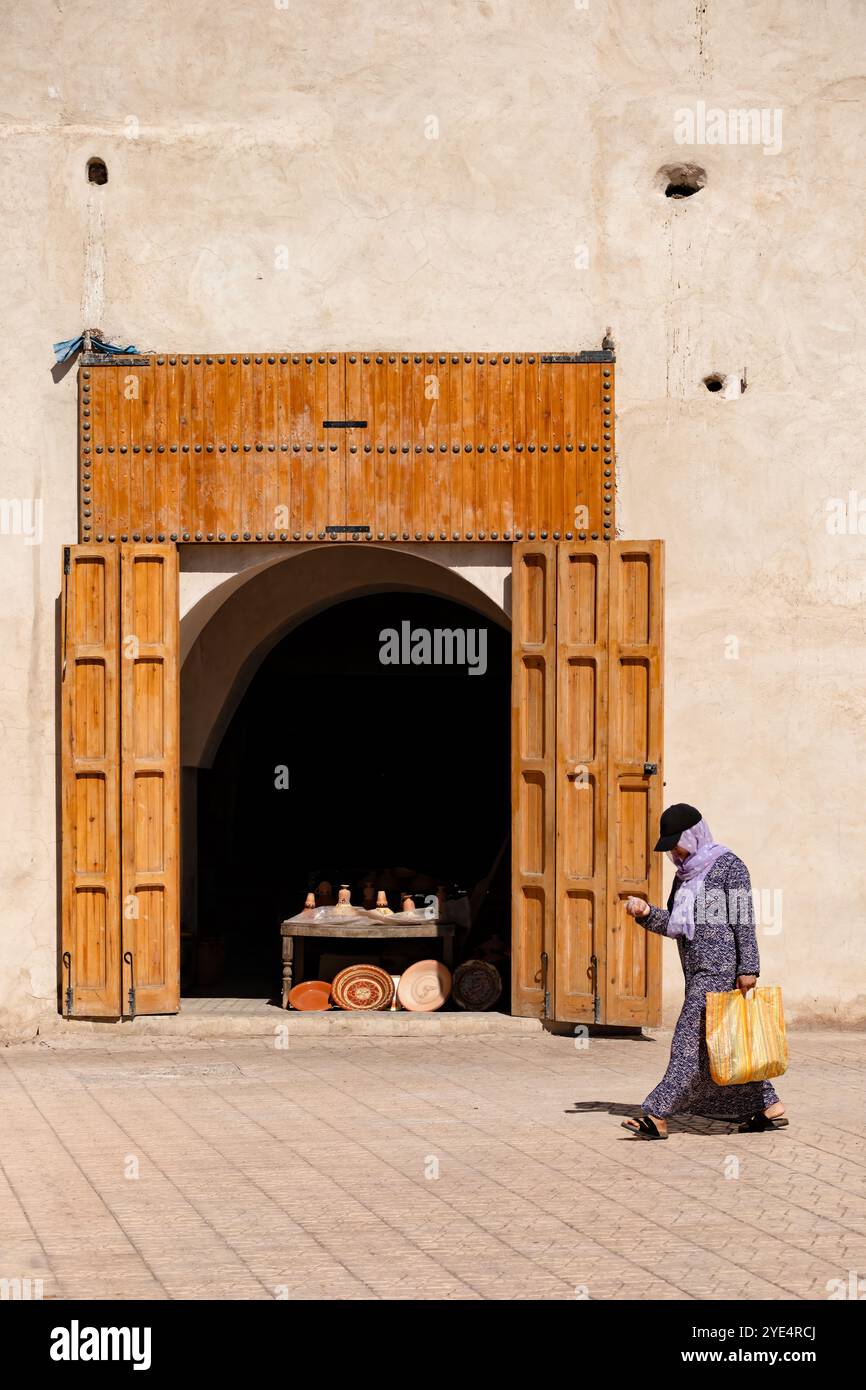 Marrakesch Marokko. Eine Frau läuft an einer handwerklichen Töpferei in der Medina vorbei, die Töpferschalen und Geschirr verkauft, die im Ladeneingang ausgestellt werden Stockfoto