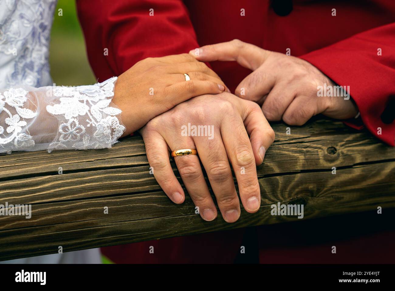 Hände der Braut und des Bräutigams mit Ringen auf Holzbräutigam im roten Anzug Stockfoto