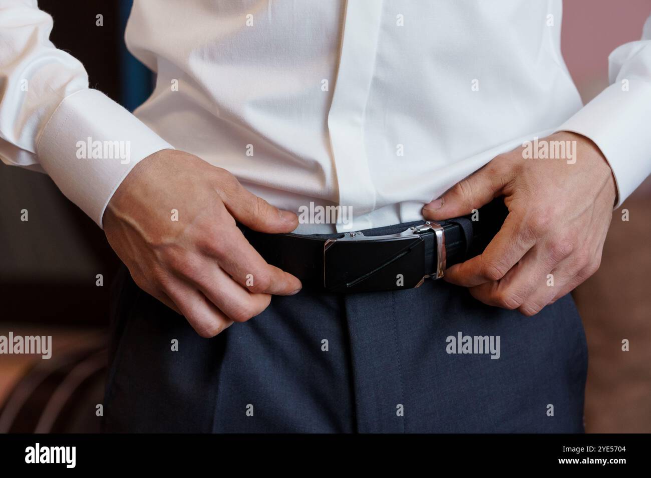 Eleganter Mann, der seinen Gürtel in einem maßgeschneiderten Anzug verstellt. Stockfoto