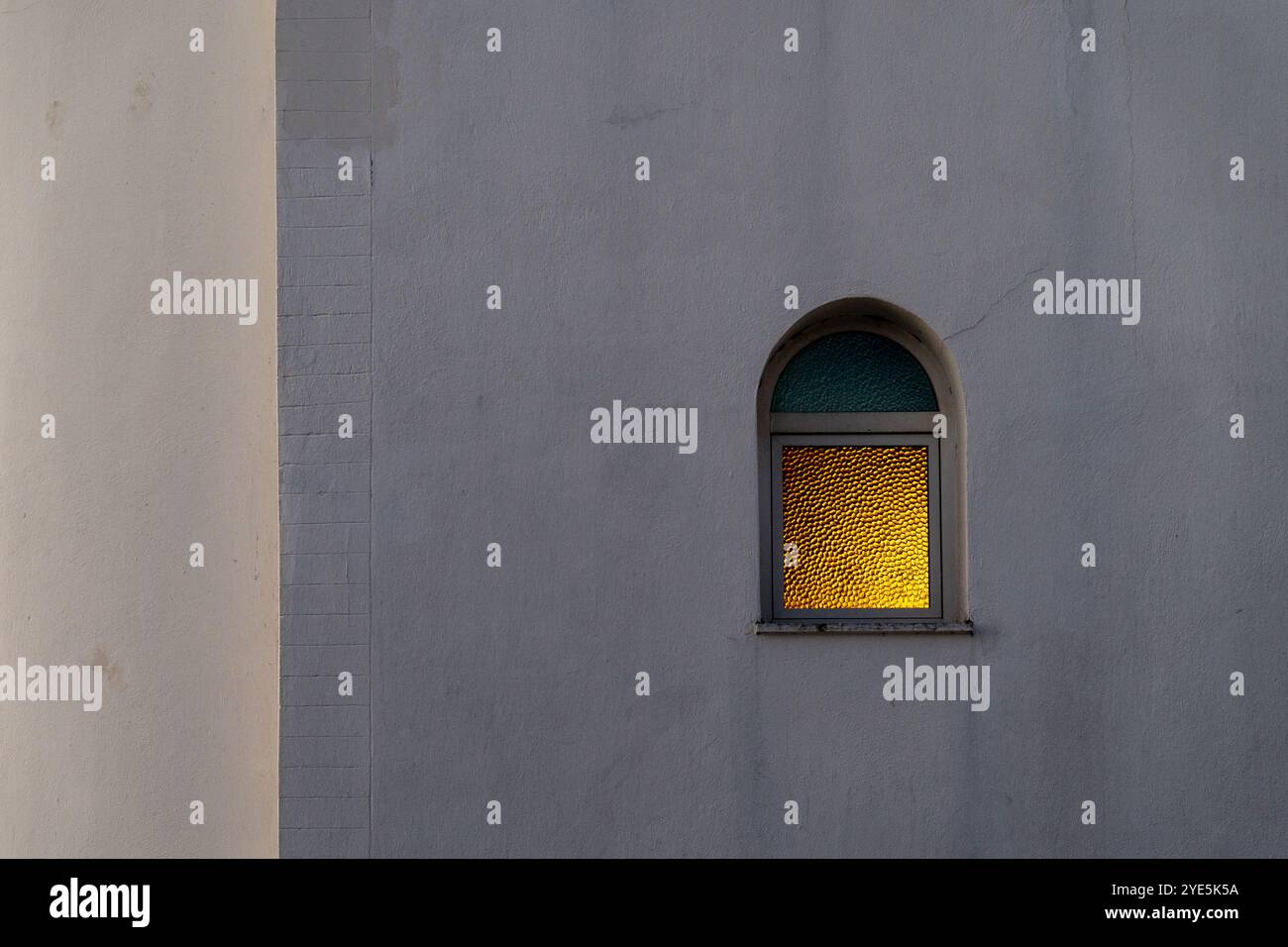 Radiant Arch: Gelb leuchtender Fensterrahmen auf der Weißen Wand einer Kirche Stockfoto