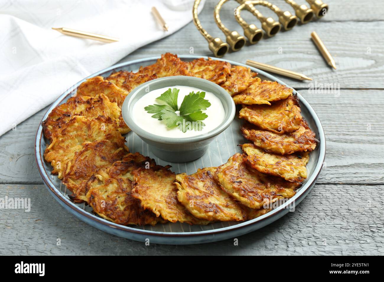 Leckere Kartoffelpfannkuchen, Menora und Kerzen auf grauem Holztisch, Nahaufnahme. Hanukkah festliches Essen Stockfoto