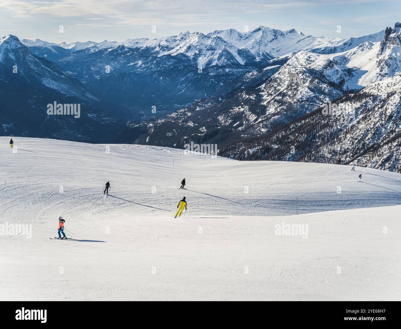 Skifahrer gleiten auf einem sanften, schneebedeckten Berghang, umgeben von landschaftlich reizvollem alpinen Gelände. Das Bild erfasst den offenen Raum, den frischen Schnee und die Weite Stockfoto