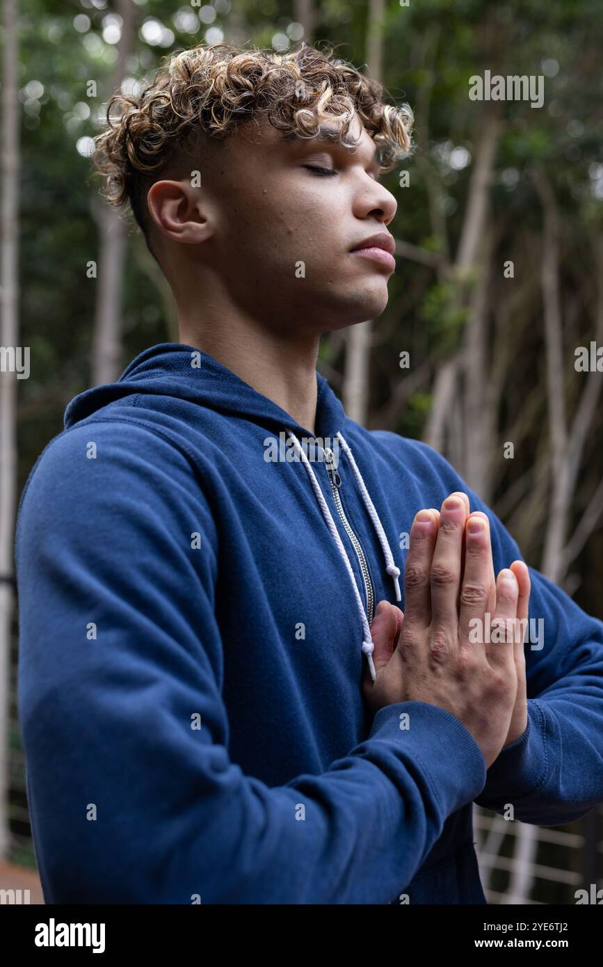 Junger Mann, der auf dem Balkon im friedlichen Wald meditiert, mit blauem Hoodie Stockfoto