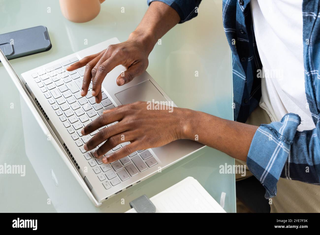 afroamerikanischer Mann, der zu Hause auf einem Laptop tippt, mit Smartphone und Kaffee in der Nähe arbeitet Stockfoto