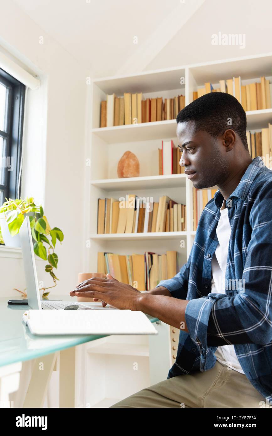 Fokussierter afroamerikanischer Mann, der im Heimbüro mit Bücherregalen arbeitet Stockfoto