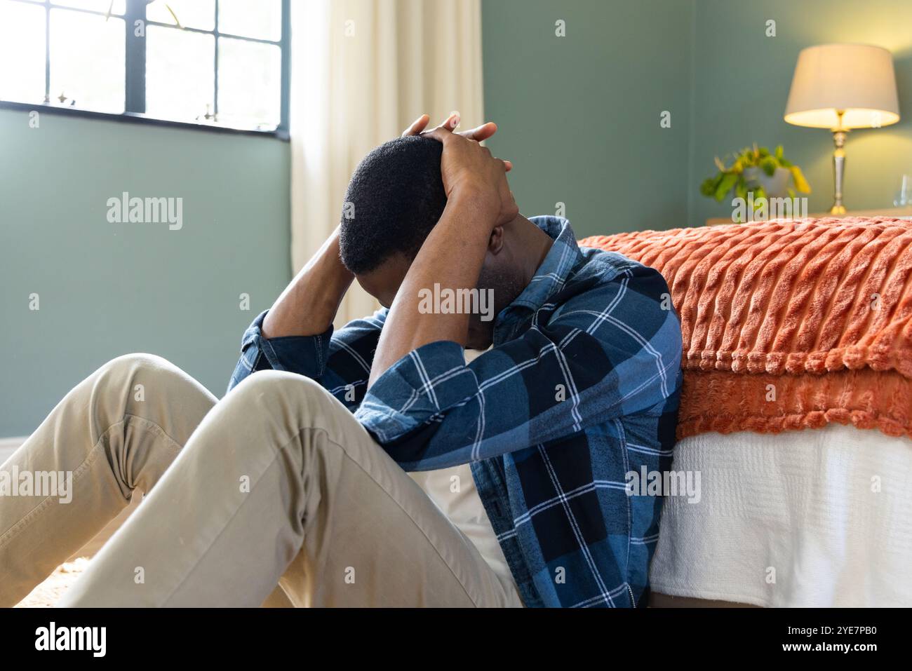 Afroamerikaner sitzt auf der Schlafzimmeretage, sieht gestresst und überfordert aus, zu Hause Stockfoto
